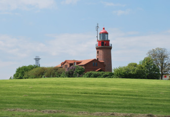 View of the red lighthouse and lodge 'Am Strand' in Germany with green grass and a clear blue sky.