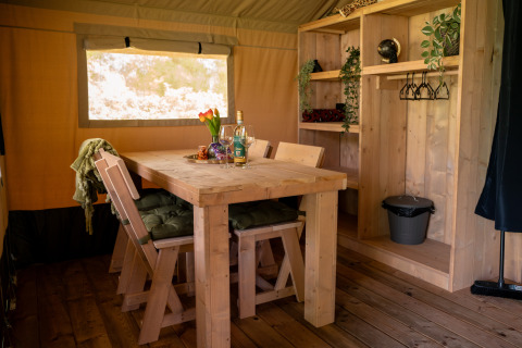 Innenraum des Forest Lodge Safari-Zelts im Jocomo Parc, Belgien, mit Holzmöbeln und Esstisch.