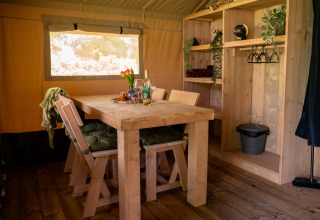 Intérieur de la tente safari Forest Lodge au Jocomo Parc en Belgique, avec table en bois et étagères ouvertes.