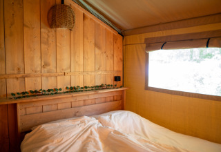 Interieur van de Forest Lodge safaritent in Jocomo Parc, België, met houten wand en bed.