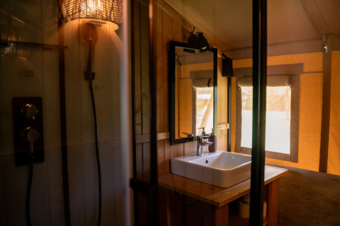 Modernes Badezimmer in einem Safarizelt mit Waschbecken, Spiegel, Dusche und Sonnenlicht am Fenster.