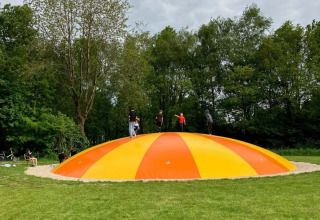 Bambini che giocano su un grande cuscino gonfiabile arancione e giallo al campeggio de Bouwte, Groningen.