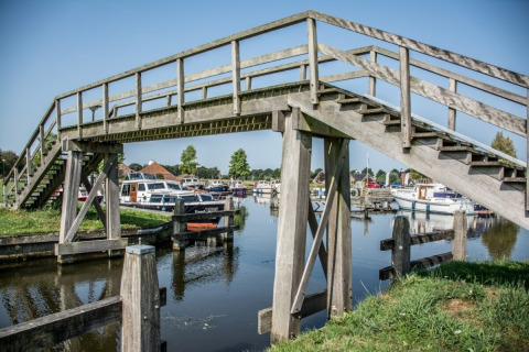 Wooden pedestrian bridge over a canal with boats, near Midwolda, Groningen, Netherlands on a sunny day.