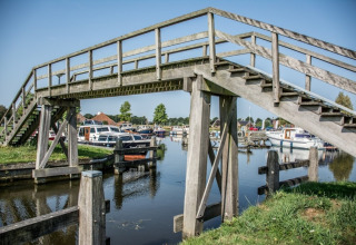 Ponte pedonale in legno sopra un canale con barche vicino a Midwolda, Groningen, Paesi Bassi in una giornata di sole.