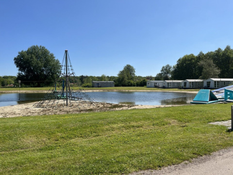 Campsite de Bouwte in Groningen, Netherlands, featuring a climbing frame, pond, and holiday cabins on a sunny day.