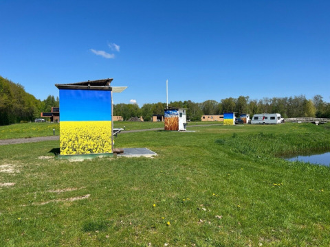 Campsite de Bouwte in Groningen, Netherlands, with painted huts, grassy field, and blue sky view.
