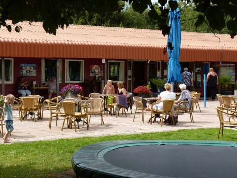 Outdoor café area at Campsite de Bouwte in Groningen with guests seated, tables, and children playing.
