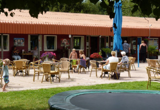 Outdoor café area at Campsite de Bouwte in Groningen with guests seated, tables, and children playing.