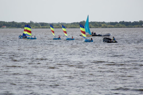 Colorful sailboats on the water near Midwolda, Groningen, Netherlands, with a green shoreline in the distance.