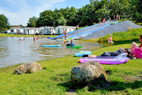 Holiday park in Groningen, Netherlands, with lake, water slide, children playing and people relaxing.