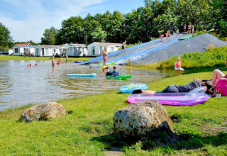 Vakantiepark in Groningen, Nederland met vijver, glijbaan en mensen die genieten van hun vrije tijd.