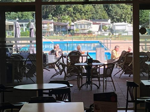 View from inside a café at San Lanaco campsite in Belgian Limburg, overlooking outdoor seating and the pool.