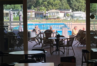 View from inside a café at San Lanaco campsite in Belgian Limburg, overlooking outdoor seating and the pool.