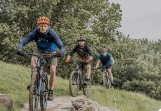 Tre ciclisti pedalano su mountain bike tra la natura verde vicino a Lanaken, Belgio, circondati da alberi.