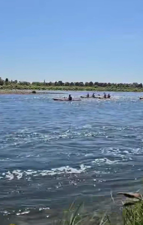 Persone in kayak su un fiume vicino a Lanaken, Limburgo belga, circondate da vegetazione e cielo azzurro.