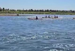 Persone in kayak su un fiume vicino a Lanaken, Limburgo belga, circondate da vegetazione e cielo azzurro.