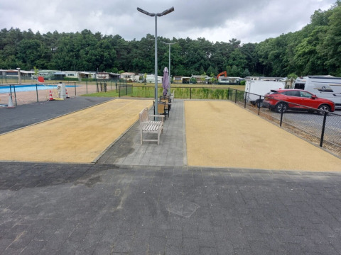 Foto del campeggio San Lanaco in Belgio con panchine, corsie di sabbia, auto e roulotte sullo sfondo.