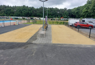 Photo of Campsite San Lanaco in Belgium with benches, sand lanes, parked cars and caravans in the background.