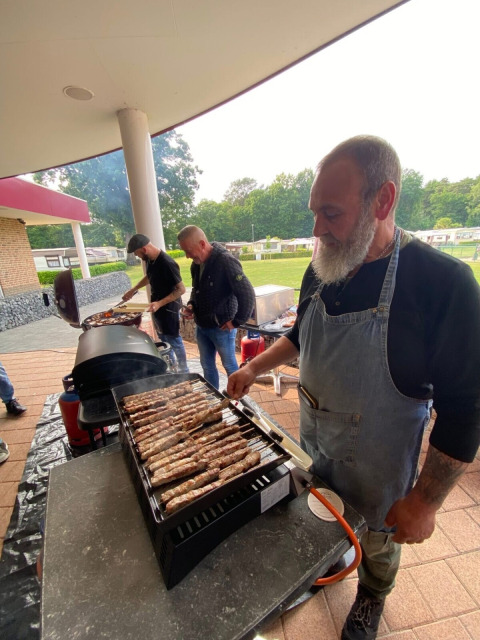 Uomini che grigliano cibo all'aperto sotto una tettoia al campeggio San Lanaco nel Limburgo belga.