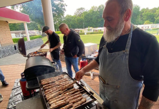 Uomini che grigliano cibo all'aperto sotto una tettoia al campeggio San Lanaco nel Limburgo belga.