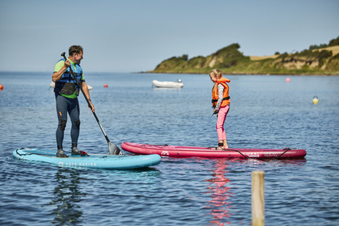 Due persone fanno paddleboard sull’acqua a Emmerbølle Strand Camping in una giornata di sole.