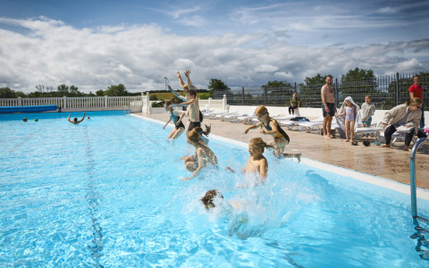 Bambini saltano in piscina a Emmerbølle Strand Camping, Danimarca, mentre persone li osservano a bordo vasca.