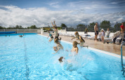 Kinder springen in einen Pool im Emmerbølle Strand Camping, während Erwachsene am Beckenrand zuschauen.