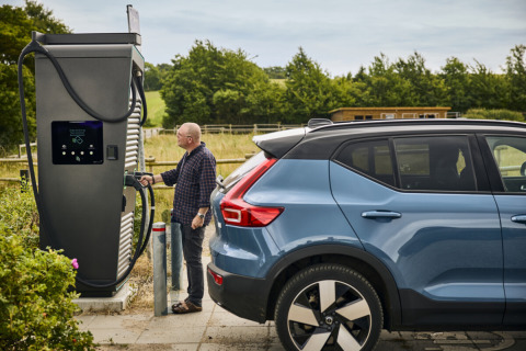 Uomo ricarica auto elettrica presso stazione a Emmerbølle Strand Camping, sud Danimarca, in mezzo al verde.