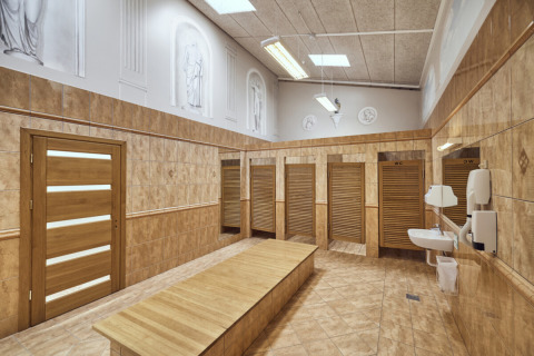 Un vestuario moderno en Emmerbølle Strand Camping con puertas de madera, bancos y lavabos en la pared.