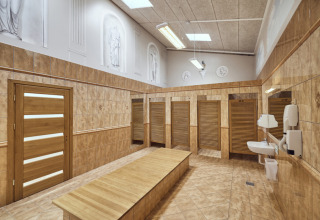 Een moderne kleedkamer bij Emmerbølle Strand Camping met houten deuren, banken en wastafels langs de muur.