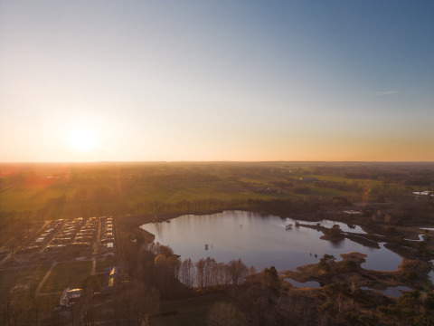 Prachtige zonsondergang boven een gezellige glampingplek aan een meer, met uitzicht op het platteland.