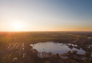 Smuk solnedgang over et naturskønt glamping-sted ved en sø med grønne marker i baggrunden.