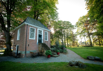 Sfeervolle glamping-accommodatie met een klein bakstenen huisje, omringd door bomen en groen grasveld.