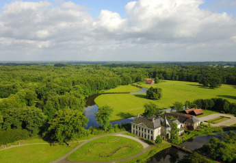 Luchtfoto van een luxe glamping-accommodatie omringd door bossen, groene velden en een kronkelende rivier.