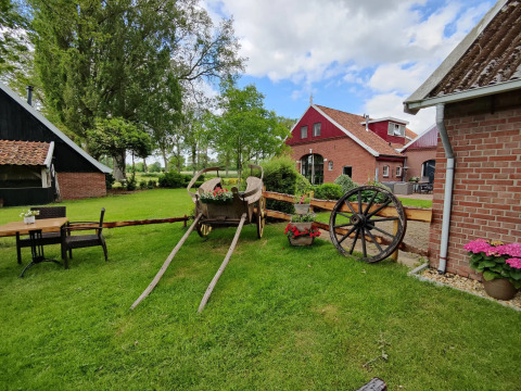 Country glamping accommodation featuring a rustic wheelbarrow, flowers, and charming farmhouses nearby.
