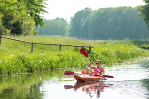 Vater und Sohn paddeln gemeinsam im Kajak auf einem ruhigen Fluss nahe einer Glamping-Unterkunft.