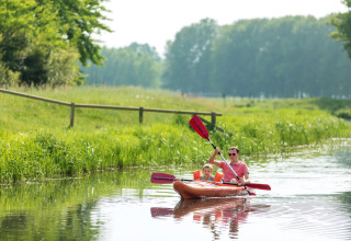 Father and son enjoy kayaking on a calm river surrounded by greenery at a scenic glamping site.