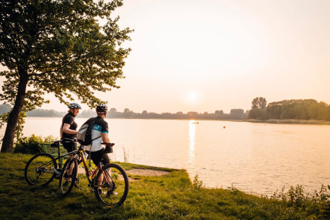 Zwei Radfahrer blicken bei Sonnenuntergang über einen See nahe ihrer Glamping-Unterkunft.