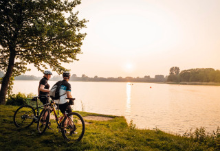 Zwei Radfahrer blicken bei Sonnenuntergang über einen See nahe ihrer Glamping-Unterkunft.