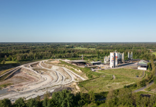 Luftaufnahme einer Glamping-Unterkunft mit Campingplatz, Industrieanlagen und grüner Landschaft.