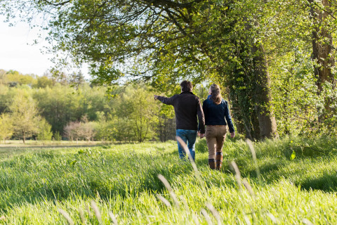 Zwei Menschen spazieren Hand in Hand durch das grüne Gelände einer Glamping-Unterkunft im Frühling.