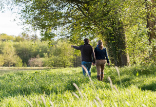 Zwei Menschen spazieren Hand in Hand durch das grüne Gelände einer Glamping-Unterkunft im Frühling.