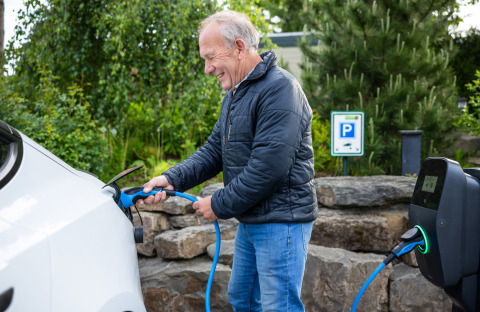 Uomo ricarica un'auto elettrica alla stazione di ricarica presso il Campeggio Roland, Limburg, Paesi Bassi.