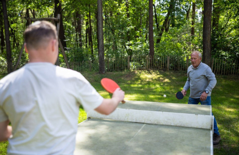 Two men play outdoor table tennis at Campsite Roland, a holiday park in Limburg, Netherlands, in nature.