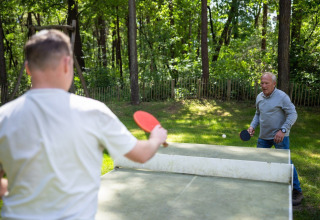 Two men play outdoor table tennis at Campsite Roland, a holiday park in Limburg, Netherlands, in nature.