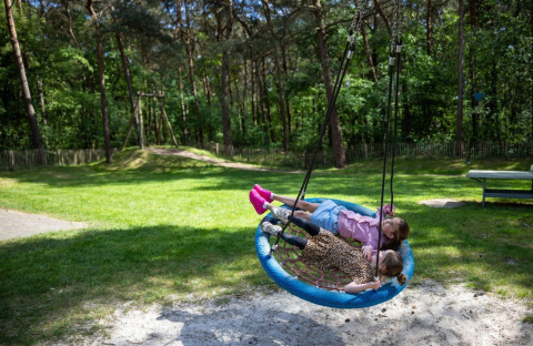 Two children lying on a round swing in a grassy area at Campsite Roland holiday park in Limburg, Netherlands.