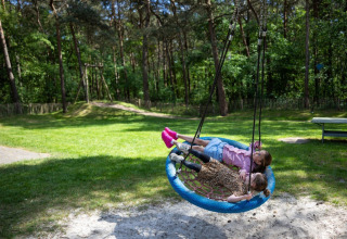 Due bambini sdraiati su un’altalena rotonda al campeggio Roland, parco vacanze in Limburg, Olanda.