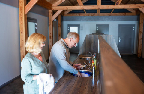 Elderly couple washing dishes together in a modern kitchen at Campsite Roland in Limburg, Netherlands.