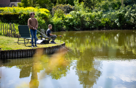 Due bambini pescano vicino a un lago al campeggio Roland, un parco vacanze in Limburg, Paesi Bassi.