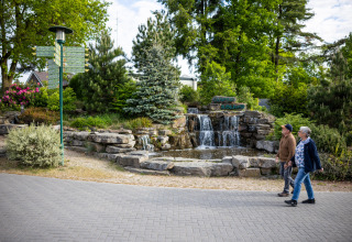 Due persone passeggiano accanto a una cascata nel verde al campeggio Roland, parco vacanze in Limburgo, Paesi Bassi.